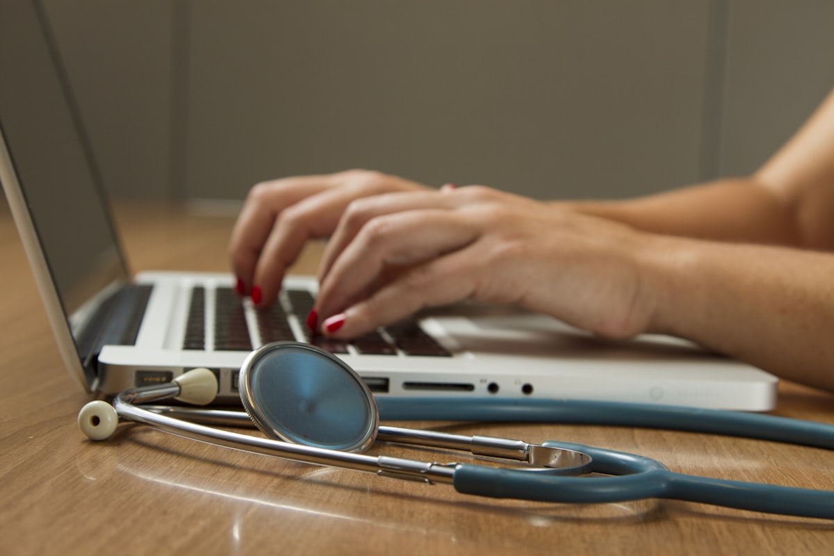 Clinician working at a laptop with a stethoscope, representing the intersection of healthcare and technology